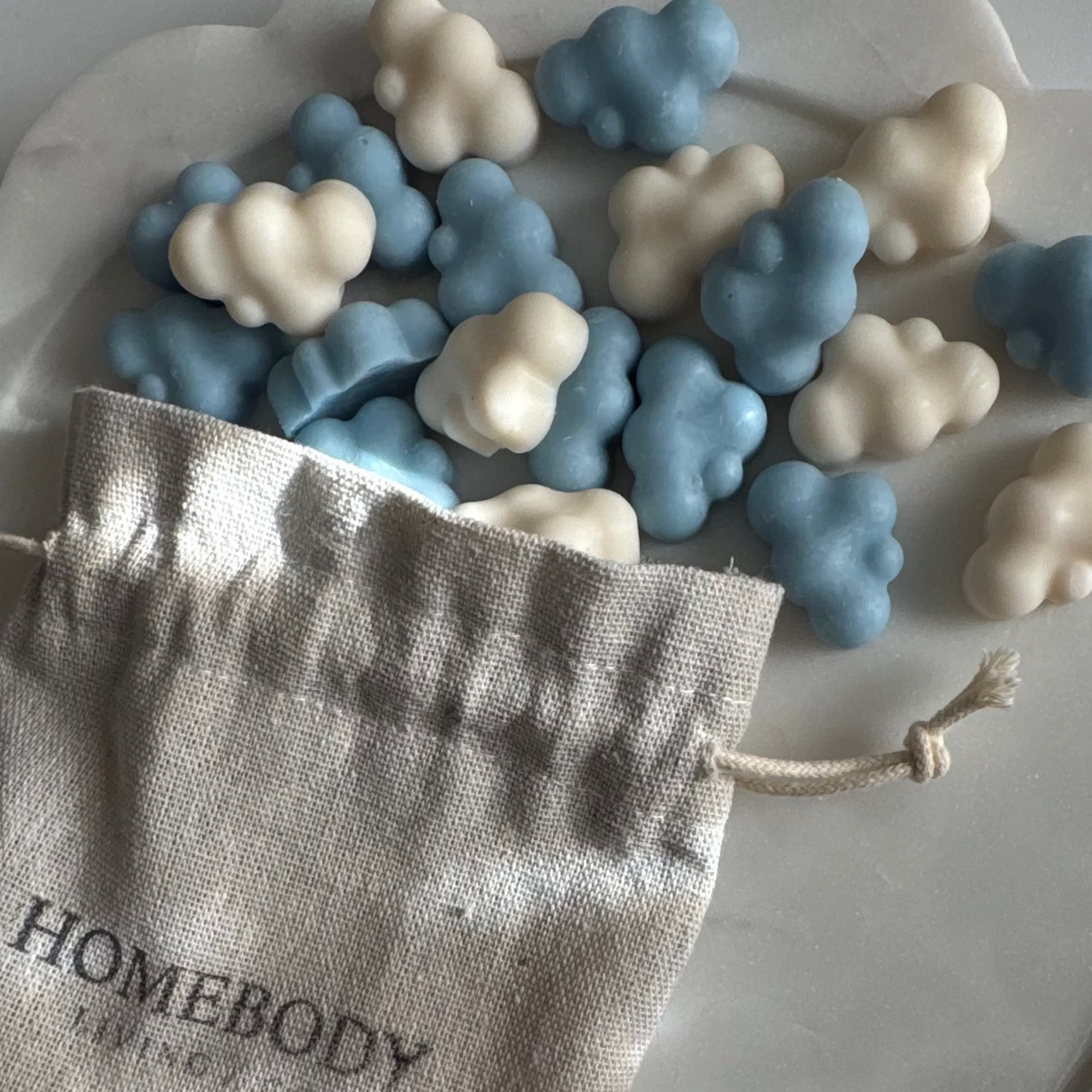 Blue and white cloud-shaped candies in a Homebody branded bag on a scalloped edge plate.